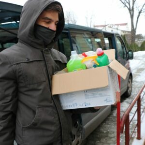 Student wnosi pudełko ze środkami czystości do budynku