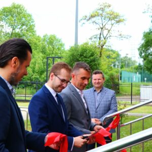 Od lewej: P. Trefler, M. Kurasz, R. Oliwa przecinają wstęgę, w tle S. Solecki