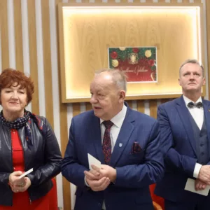 goście stojący w sali podczas spotkania opłatkowego, w rękach trzymają opłatek