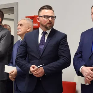goście stojący w sali podczas spotkania opłatkowego, w rękach trzymają opłatek