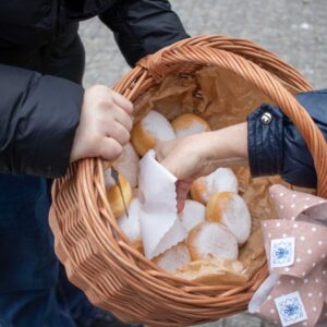 przechodzień sięga dłonią do koszyka z pączkami