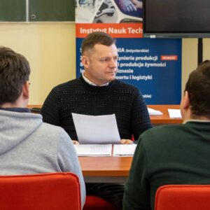 mgr inż. Rafał Hajduk przy biurku, uczniowie w ławkach