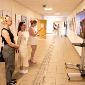 studentki oglądają film na ekranie telewizora w uczelnianym korytarzu